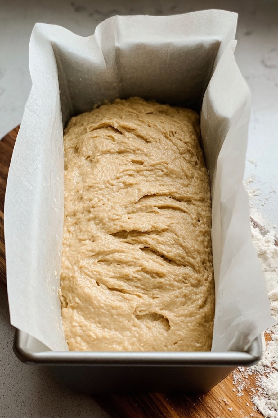 Unbaked cottage cheese banana bread batter with a textured, swirled surface, shown in a metal loaf pan lined with parchment paper and ready for the oven.