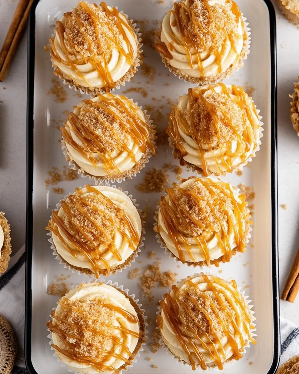 Churro Caramel Cupcakes Overhead flat lay of Churro Caramel Crunch Cupcakes on a white rectangular platter, topped with swirled cream cheese frosting, amber caramel drizzle, and cinnamon sugar coating.