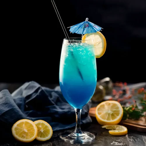 A tall, stemmed glass filled with a bright blue mocktail, garnished with a lemon slice, a blue paper umbrella, and a black straw against a dark background.