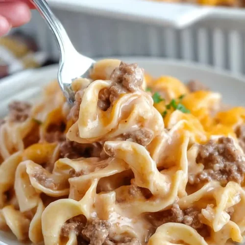 Close-up of a fork lifting a creamy bite of Hearty Amish Country Casserole, featuring tender egg noodles and savory ground beef.