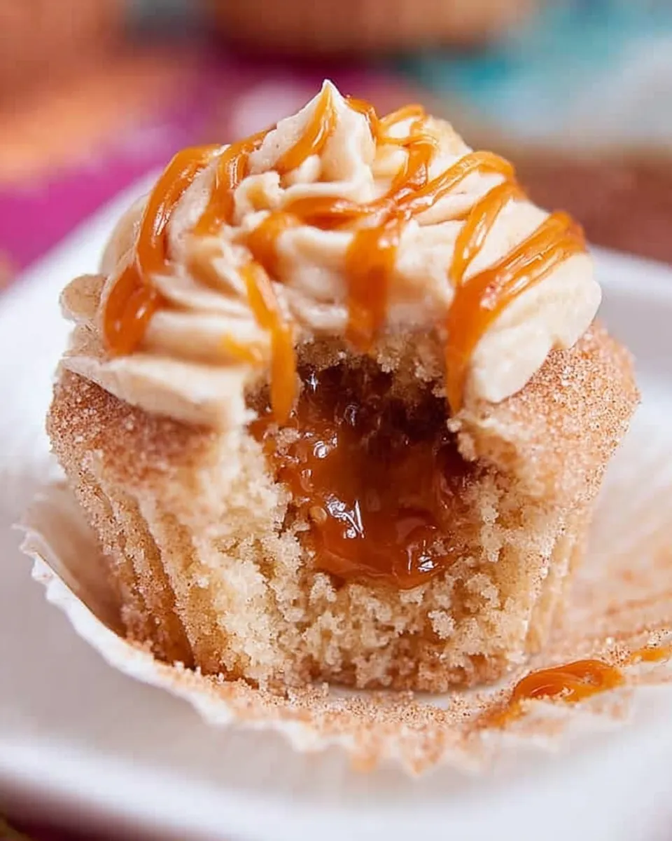 Cross-section view of a Churro Caramel Cupcake Cross-section view of a Churro Caramel Crunch Cupcake with a bite taken out, revealing the oozing homemade caramel filling center inside the cinnamon sponge.