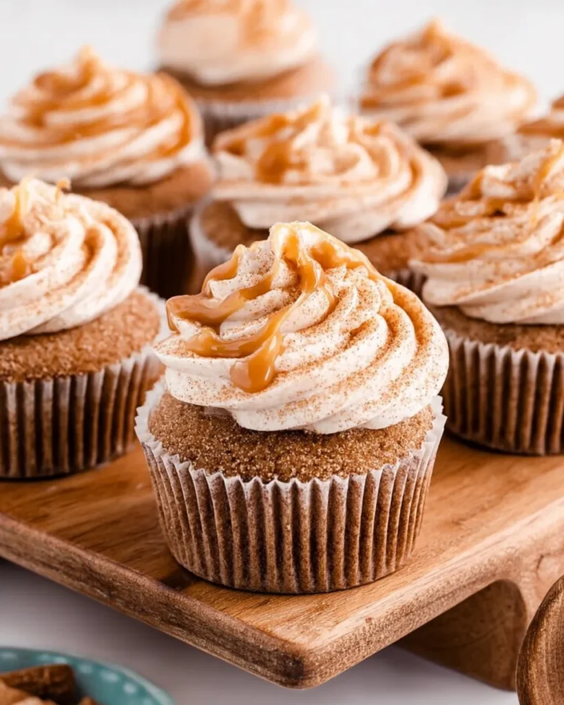 Macro close-up of a single Churro Caramel Crunch Cupcake featuring a high swirl of cream cheese frosting, a glossy caramel drizzle, and a visible cinnamon sugar coating on the cupcake rim.