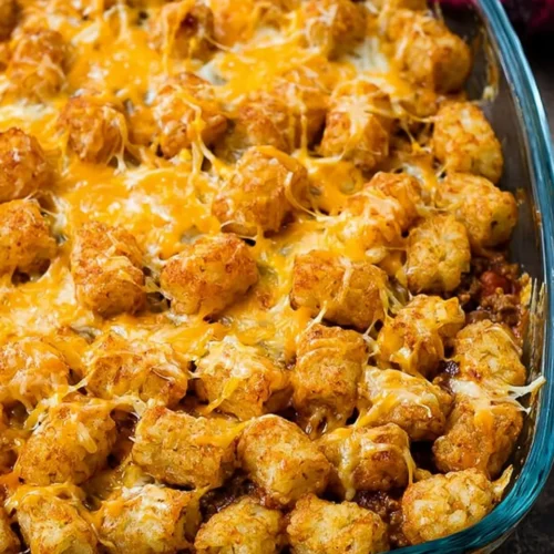 Close-up of a baked Cheesy Tater Tot Sloppy Joe Skillet in a glass dish, featuring golden crispy tater tots and melted cheddar cheese over a savory ground beef filling.