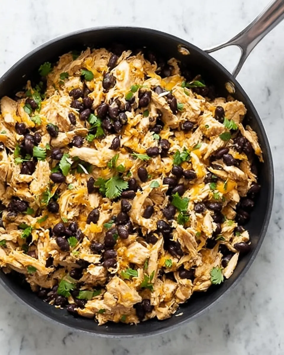 Skillet filled with seasoned shredded chicken, black beans, and fresh cilantro ready for enchilada casserole assembly.
