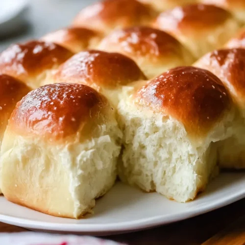 Close-up of baked small batch yeasted rolls on a white plate, showing the soft, fluffy white interior of a pulled-apart roll and glossy golden tops.