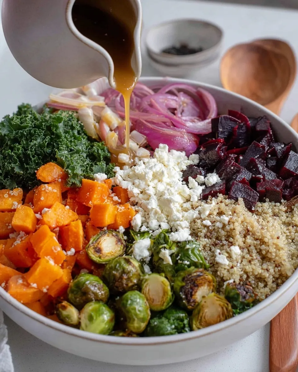 Close-up action shot of golden honey-orange dressing being poured from a white pitcher over a bowl of Quinoa Salad with Roasted Vegetables, featuring distinct sections of roasted beets, butternut squash, Brussels sprouts, kale, and crumbled feta cheese.