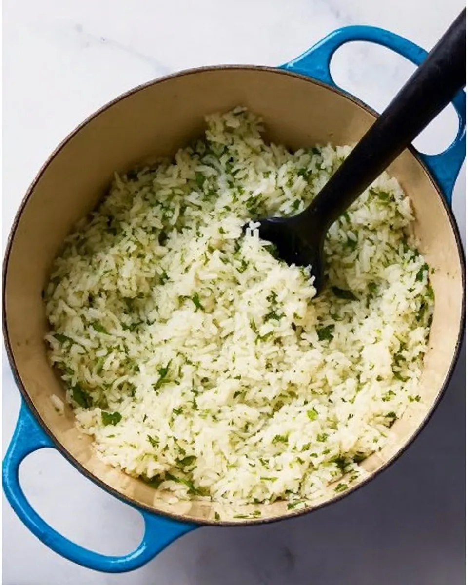 Overhead view of a blue Dutch oven filled with fluffy white rice mixed with fresh chopped cilantro and a black serving spoon.