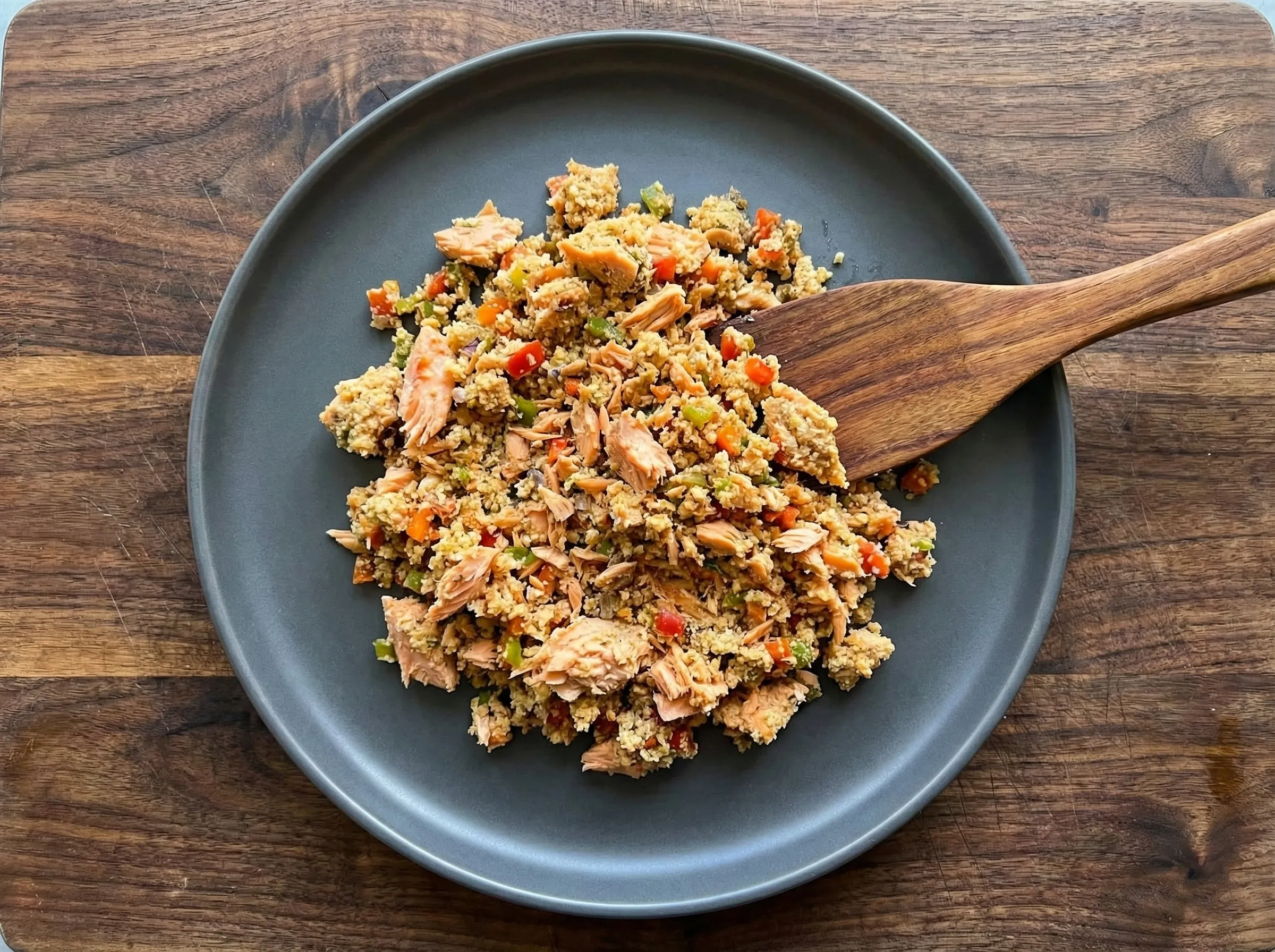 A bowl of mixed salmon cake filling showing visible chunks of red salmon, diced peppers, and panko breadcrumbs ready for shaping.