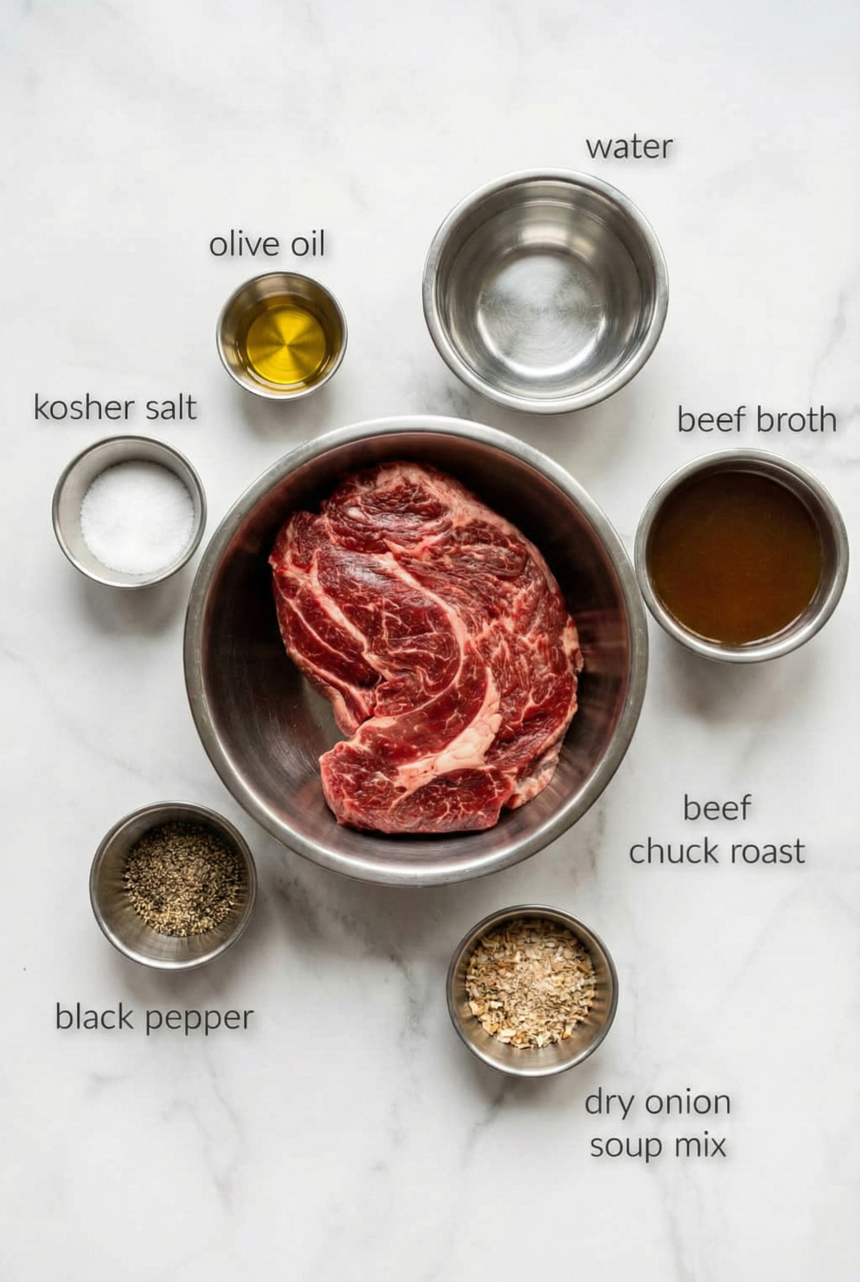 Top-down flat lay of the ingredients for Slow Cooker French Dip Sandwiches arranged on a white marble surface. Items are labeled with text and include a raw beef chuck roast, beef broth, water, dry onion soup mix, olive oil, kosher salt, and black pepper.

Caption