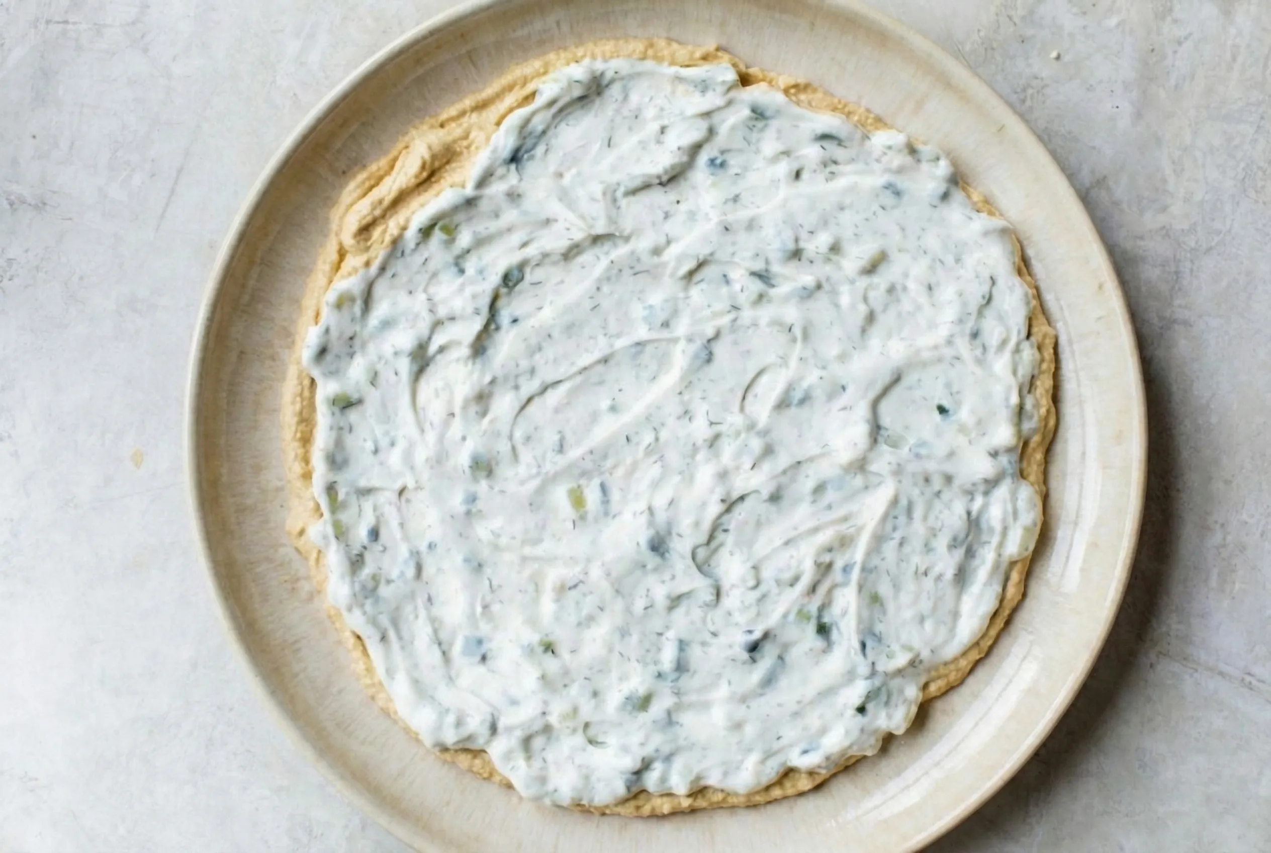 creamy white herb dip Overhead shot of a creamy white herb dip spread over a base layer of hummus on a round ceramic platter.