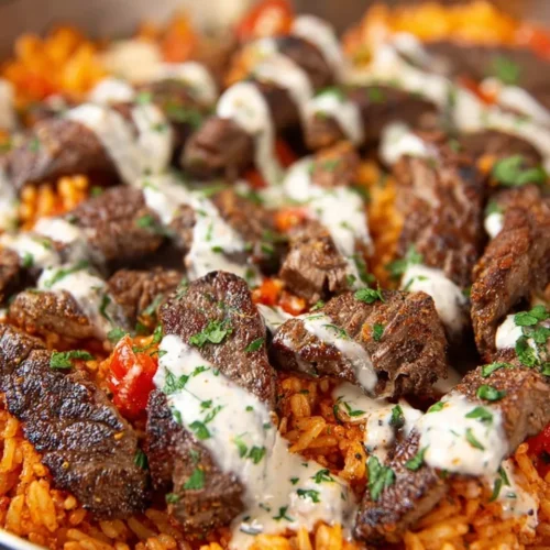 Close-up view of a skillet containing seasoned Mexican rice topped with seared sirloin steak strips, drizzled with creamy white queso sauce, and garnished with fresh chopped cilantro.