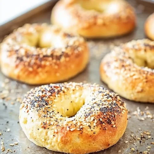 Close-up of golden brown 2-ingredient bagels topped with everything seasoning cooling on a metal baking sheet.