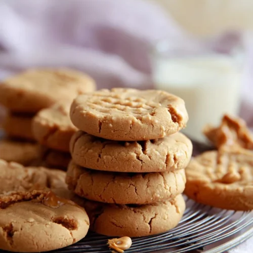 A mouthwatering stack of soft 4-ingredient peanut butter cookies resting on a wire cooling rack, with a glass of milk blurred in the background.