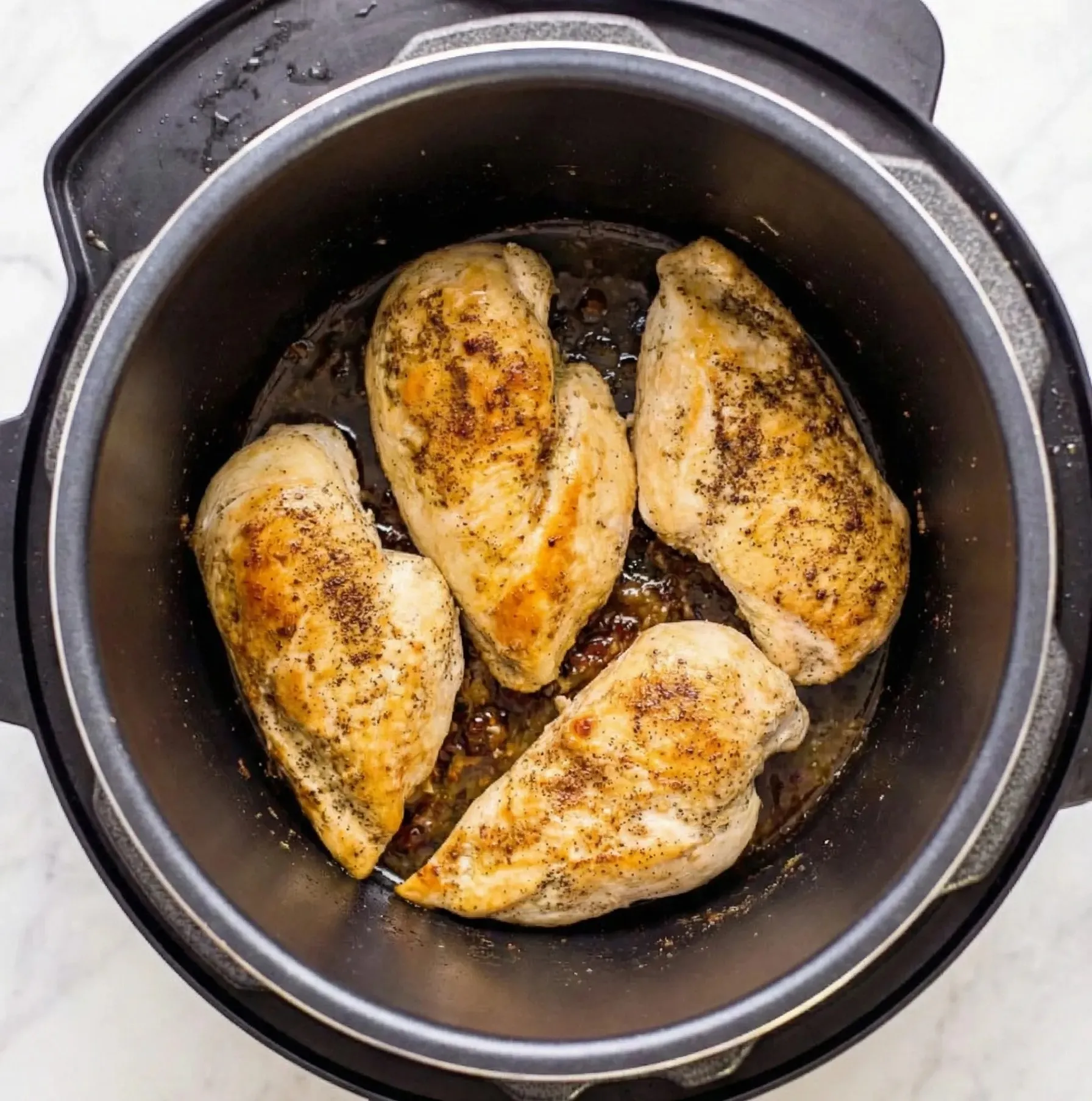 Top-down view of four cooked, seasoned chicken breasts inside a black slow cooker pot, ready to be shredded.