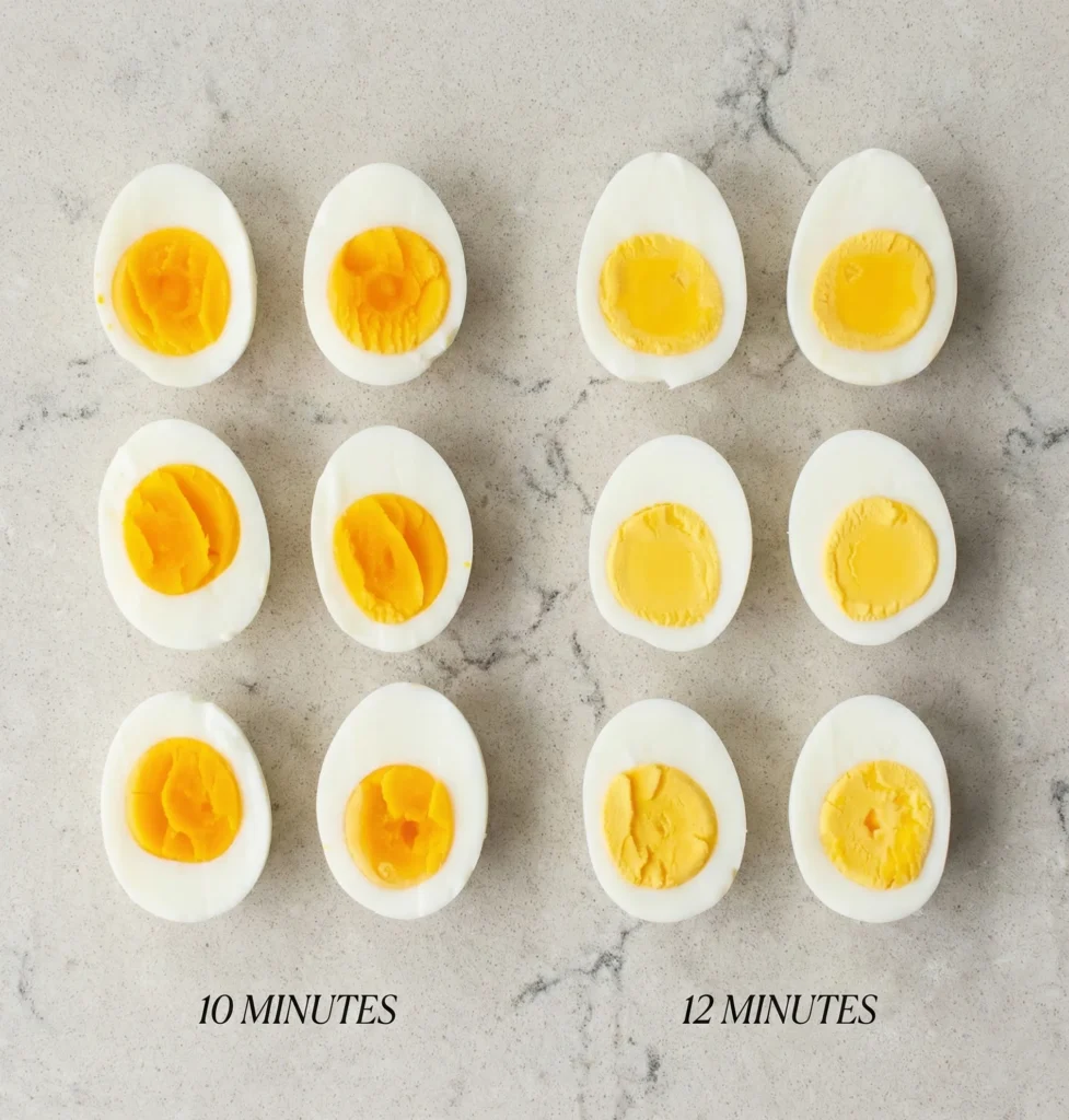 Top-down comparison of halved hard boiled eggs arranged in a grid, showing the difference between the creamy, vibrant orange yolks of 10-minute eggs versus the firm, pale yellow yolks of 12-minute eggs.
