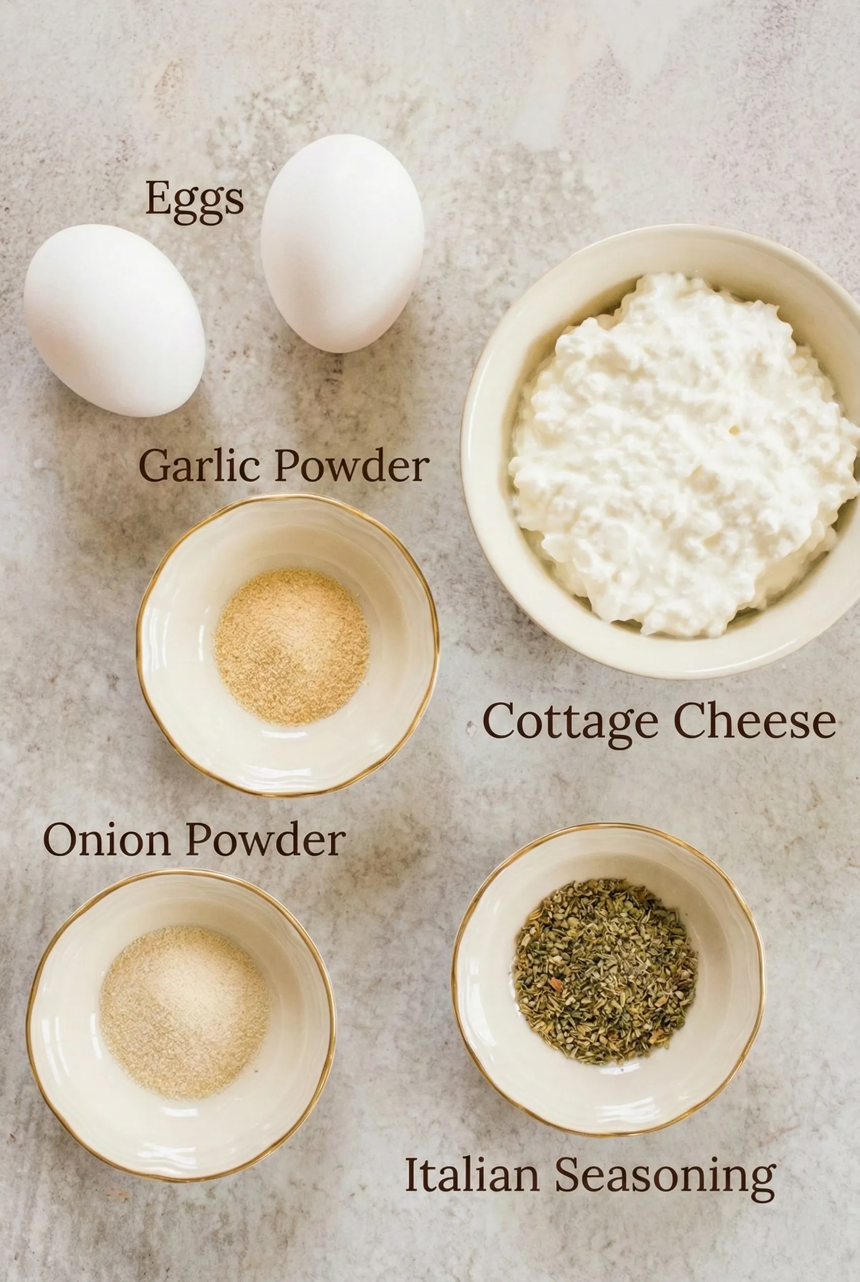 A top-down view of the ingredients needed for viral cottage cheese wraps arranged on a marble counter. Includes two white eggs, a bowl of cottage cheese, and small bowls of garlic powder, onion powder, and Italian seasoning.