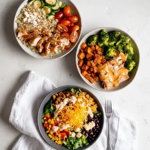 Top-down photograph of three different assembled protein power bowls arranged on a light gray surface. The top-left bowl features quinoa, sliced chicken with dark glaze, tomatoes, and cucumbers; the top-right bowl contains roasted sweet potatoes, broccoli, and salmon topped with a creamy orange sauce; and the bottom bowl is a Tex-Mex style mix with black beans, corn, greens, shredded cheese, and a creamy drizzle.