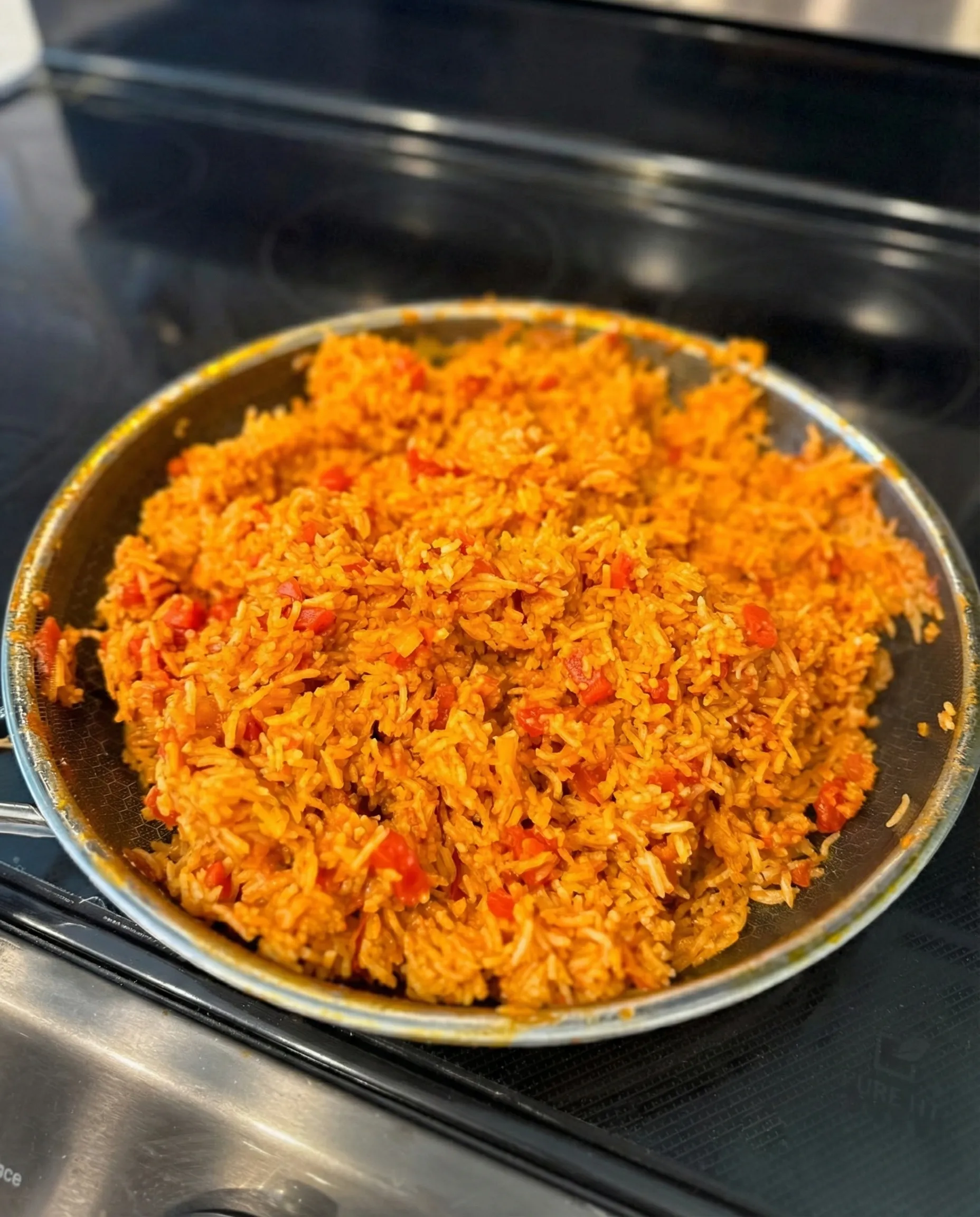 Large skillet on a stovetop filled with fluffy, seasoned Mexican rice made with crushed tomatoes and broth.