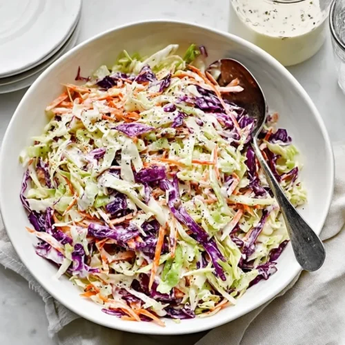 Overhead shot of a large white bowl filled with vibrant green and red cabbage and carrots, perfectly tossed in a creamy coleslaw dressing with apple cider vinegar.