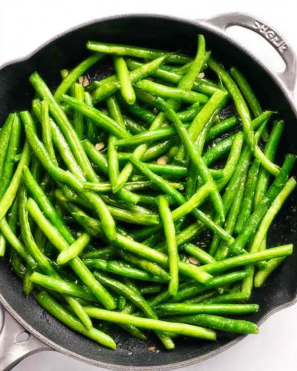 Bright, crisp green beans sautéing in a black skillet with olive oil, shallots, and minced garlic.