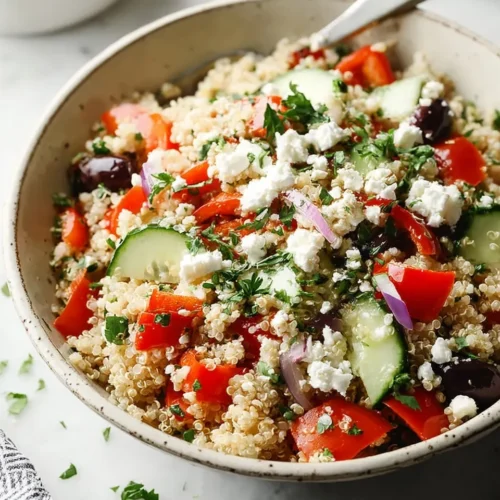 A close-up view of a freshly made Mediterranean grain salad in a rustic bowl, packed with fluffy quinoa, crisp cucumbers, vibrant tomatoes, kalamata olives, red onion, and crumbled feta cheese.