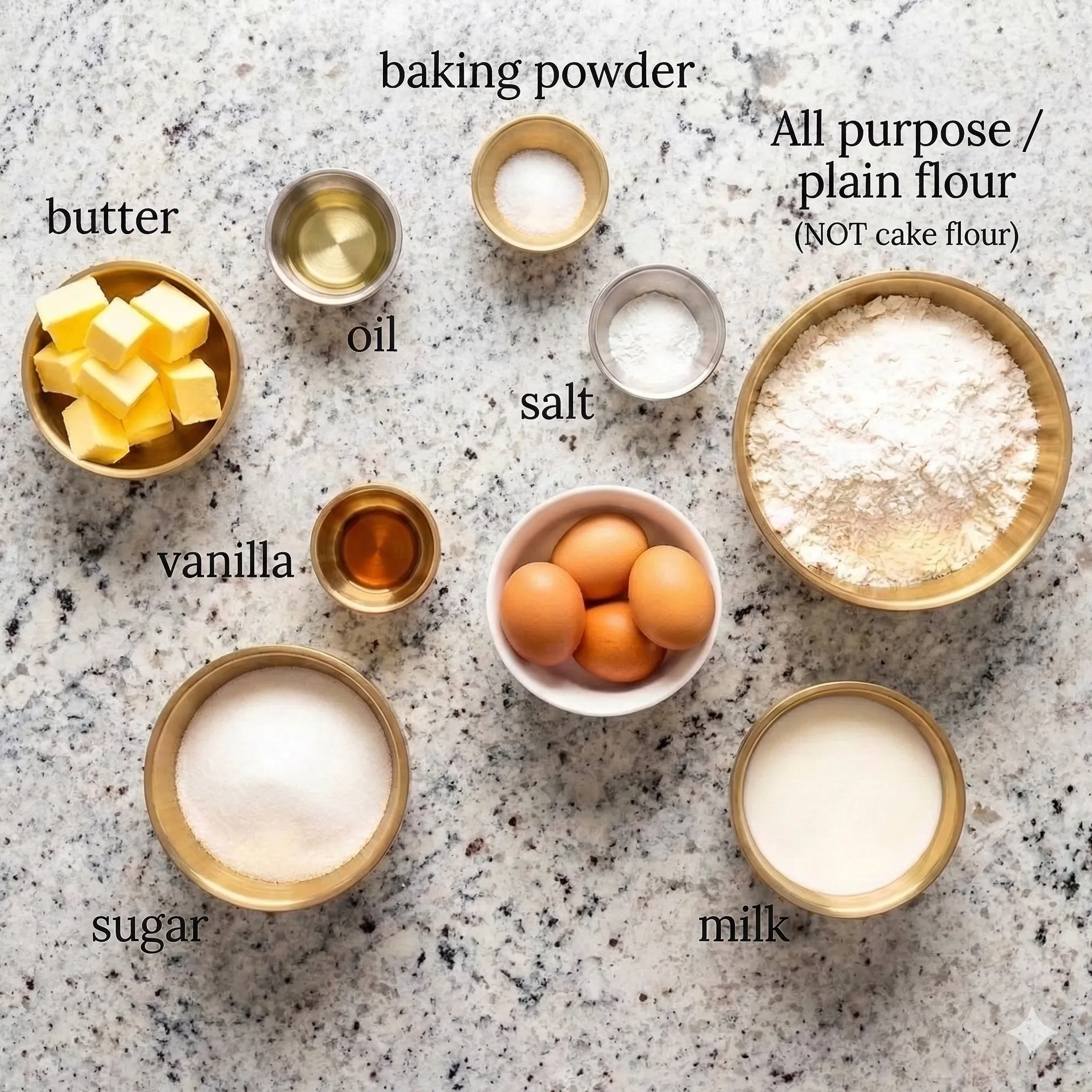 A top-down view of base batter ingredients for customizable cupcakes with frosting options, showing small bowls of cubed butter, sugar, eggs, milk, all-purpose flour, oil, vanilla, salt, and baking powder on a light speckled countertop.