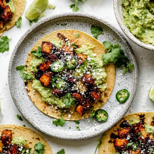 Overhead shot of a homemade street taco al pastor on a speckled plate, layered with mashed avocado, deeply caramelized meat, grilled pineapple, jalapeños, cilantro, and cotija cheese, surrounded by lime wedges and a bowl of guacamole.