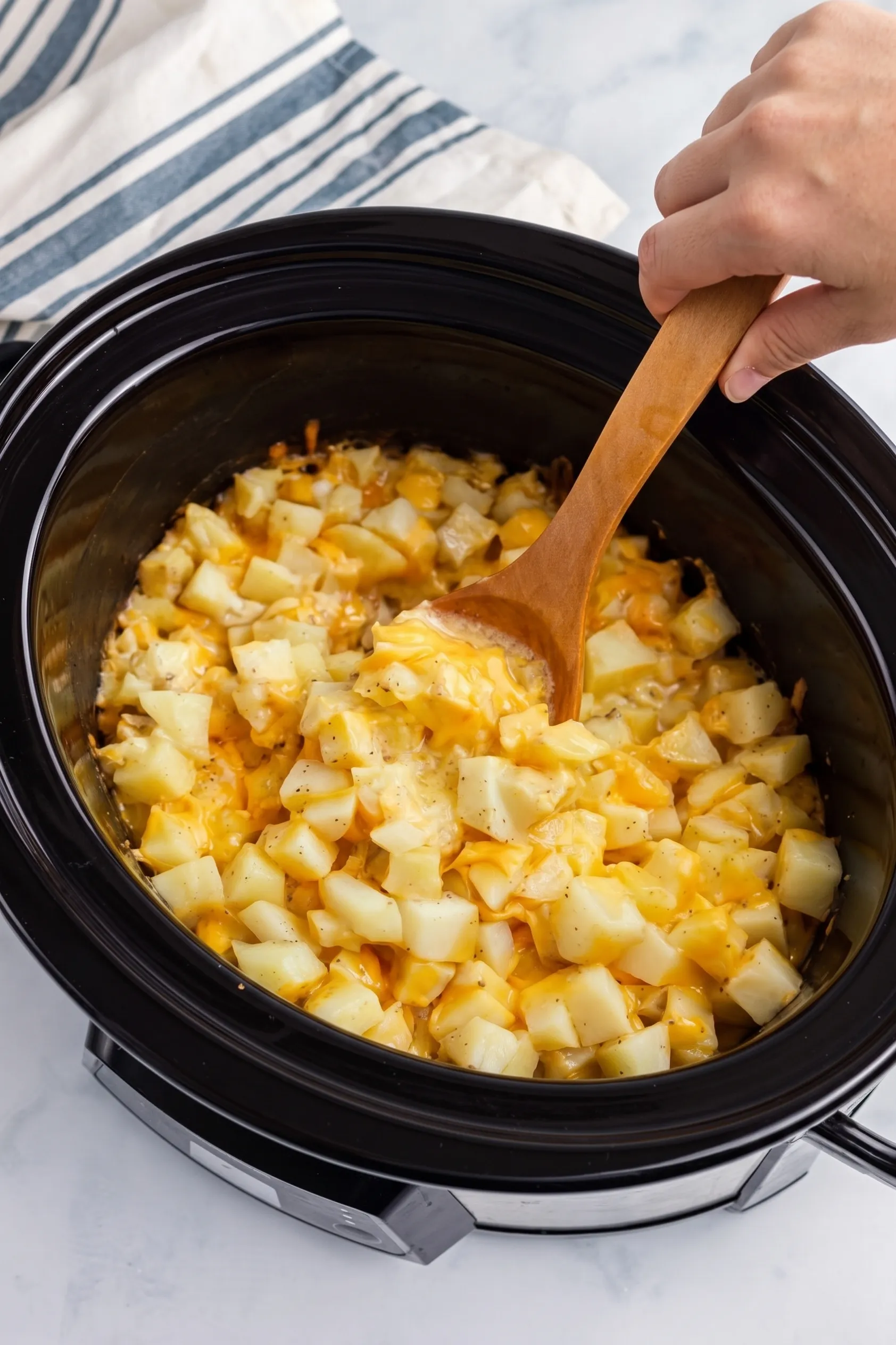 Slow-cooked cheesy potatoes with diced potatoes and melted cheese, creamy texture, served in a black crockpot.