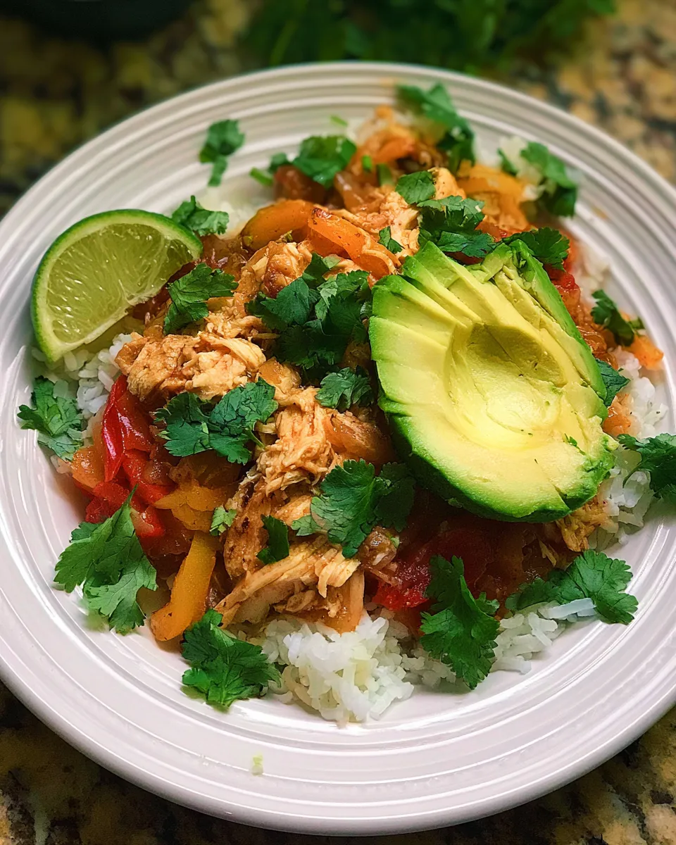 Shredded chicken with colorful bell peppers and avocado atop fluffy rice, garnished with cilantro and lime.