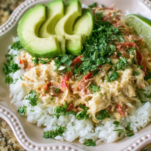 Crockpot Chicken Fajitas: shredded chicken mixed with red peppers over white rice, garnished with cilantro and avocado slices.