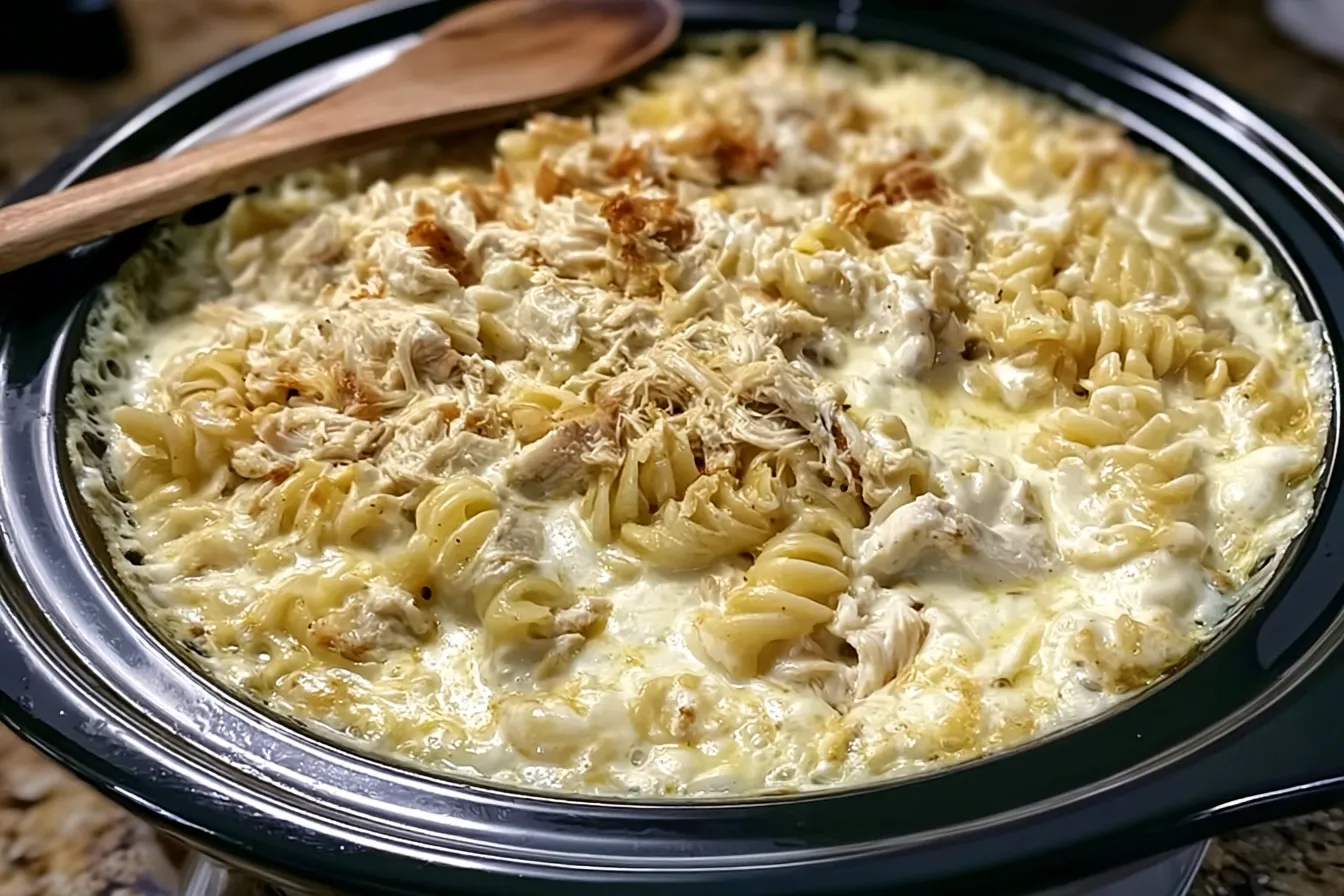 Creamy chicken pasta bake with rotini, shredded chicken, and a golden brown topping in a slow cooker.