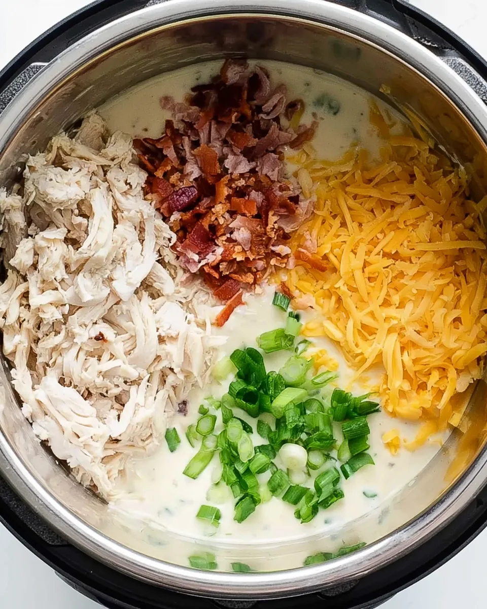 Instant Pot Crack Chicken ingredients A top-down view into an Instant Pot filled with a creamy sauce and distinct piles of shredded chicken, crumbled bacon, shredded cheddar cheese, and chopped green onions.