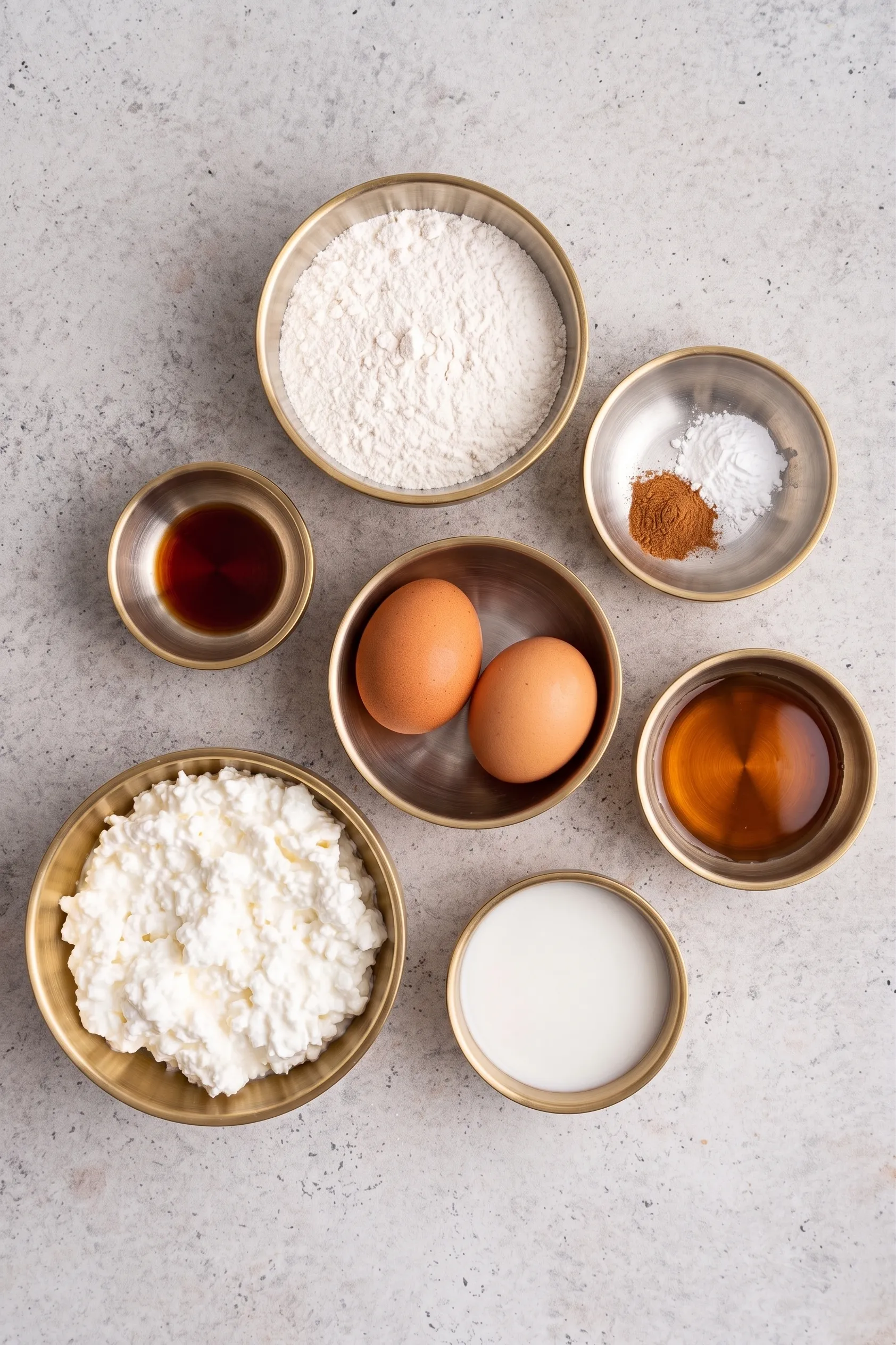 Ingredients for a baked pudding, including flour, eggs, cottage cheese, and vanilla, arranged in bowls.
