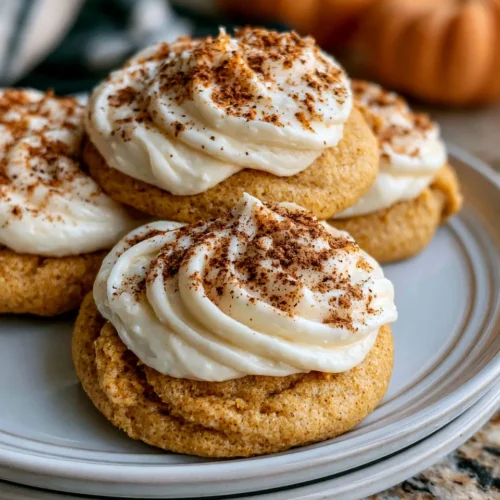 Soft pumpkin cookies topped with cream frosting and a sprinkle of cinnamon, served on a gray plate.